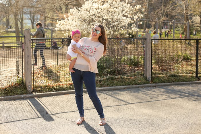 A woman in postpartum wearing skinny jeans while she holds her newborn baby in the park