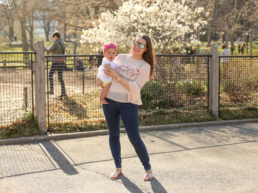 A woman in postpartum wearing skinny jeans while she holds her newborn baby in the park