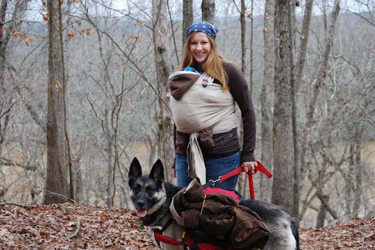 A woman in postpartum walking through the woods while carrying her baby in a baby carrier and walkin...