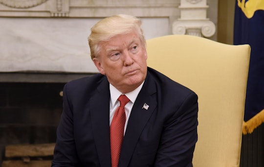 Donald Trump in a black suit, a white shirt, and a red tie sitting in a yellow chair