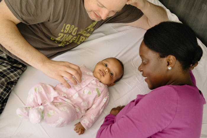A mom and dad lying on a bed with their newborn, wondering when the mother can get pregnant with the...