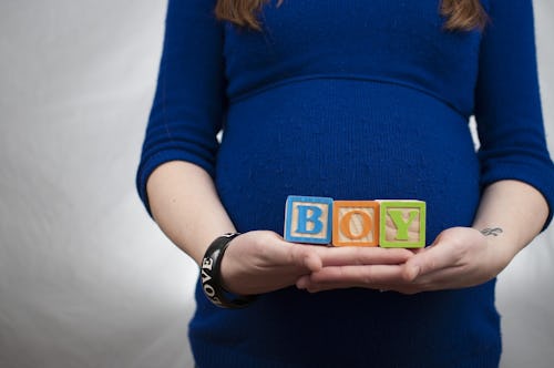 A pregnant woman holding tiny wooden boxes with b, o, and y letters