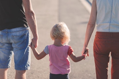 A toddler girl walking with her parents while they hold her hands