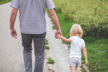 A toddler girl walks with her father while holding hands