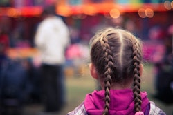 A girl with pigtails standing in front of a row of fair games