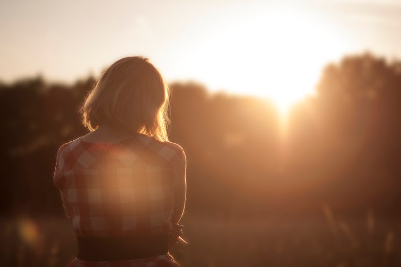 A woman standing in the middle of a field while the sun is setting.