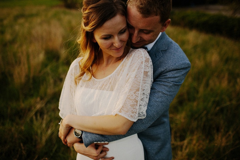 A wedding photo of a groom in a blue suit hugging a bride in a white gown in a field.