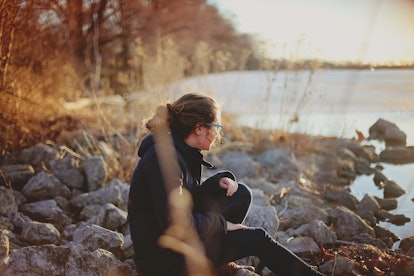 A woman wearing black sitting alone on a rocky river shore