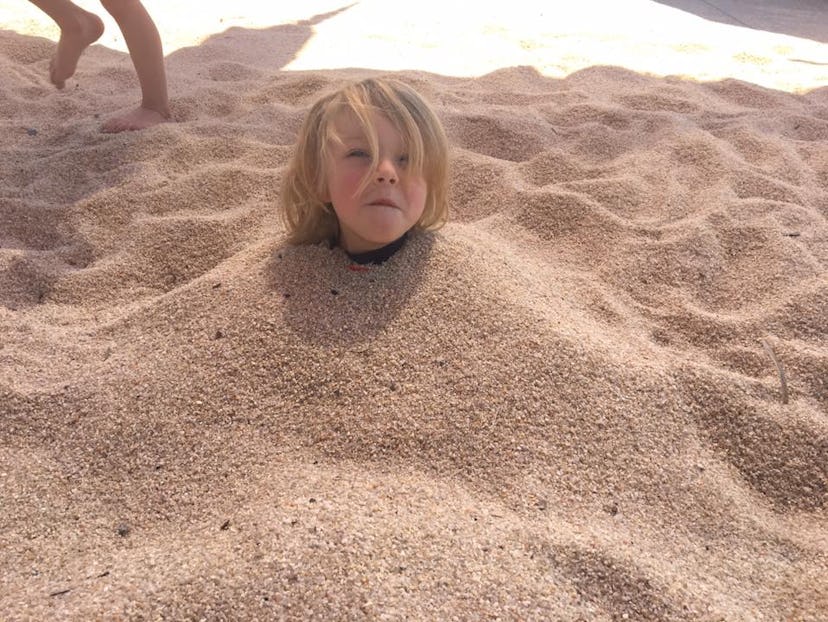 A child at the beach submerged in the sand, with only his head exposed 