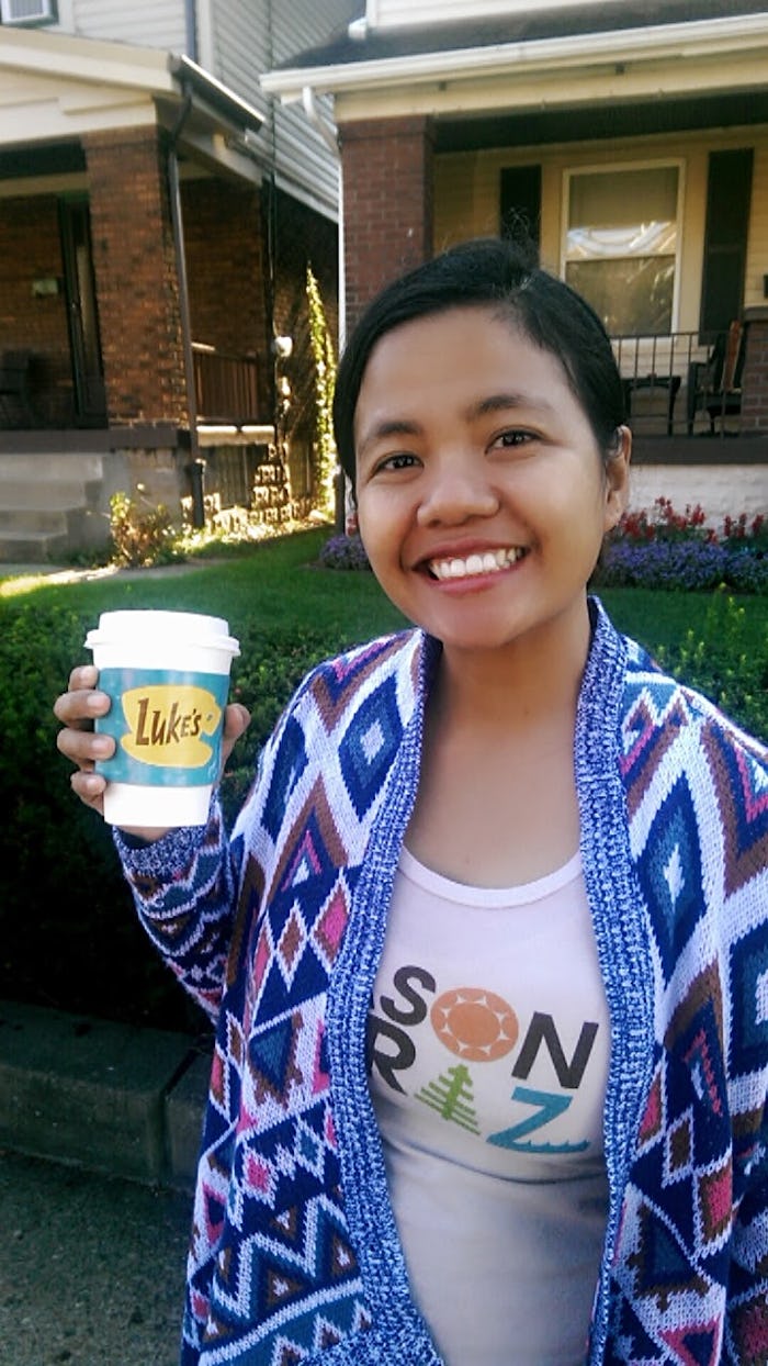 Jam Kotenko smiling in a selfie while wearing a blue-white blanket-style cardigan and a cup of coffe...