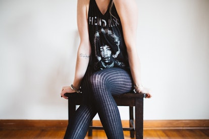 A woman wearing a band tee with Jimi Hendrix's photo and stripy leggings sitting on a stool