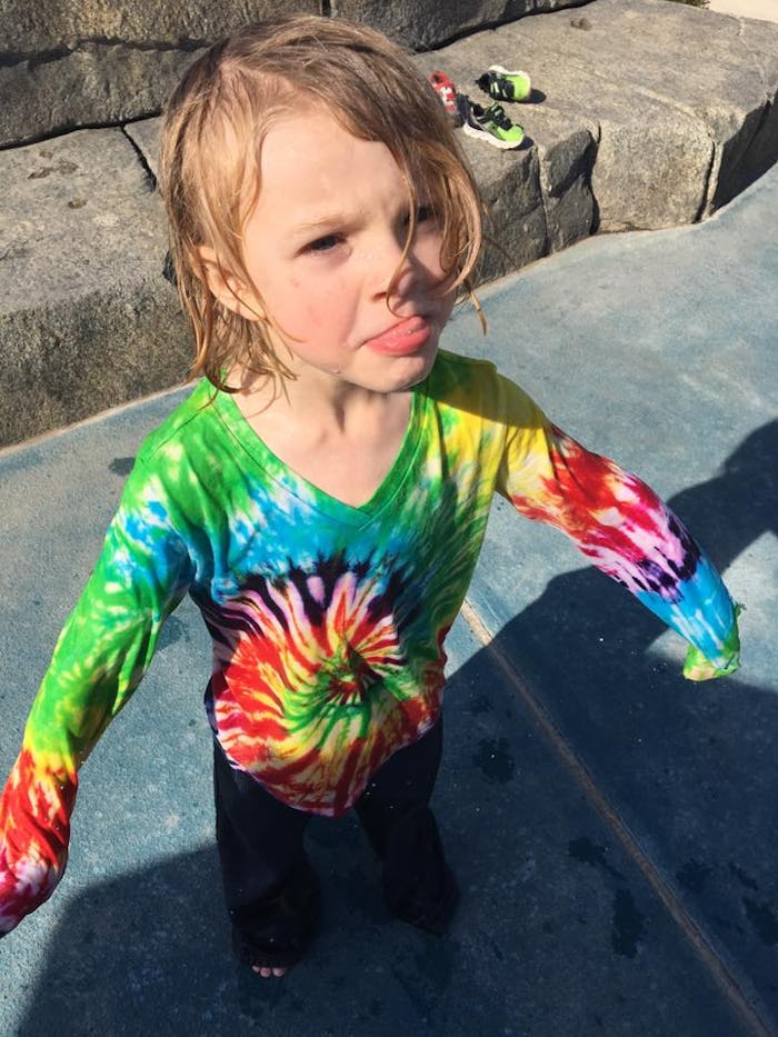 Elizabeth Broadbent's child sticking its tongue out, wearing a multi-colored tie-dye shirt