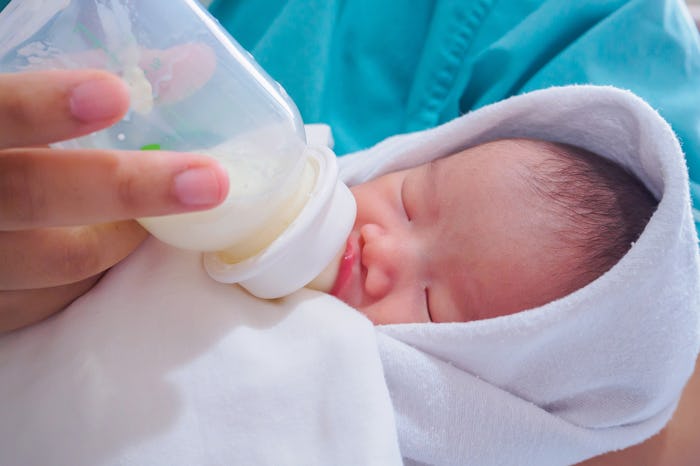 A closeup of a parent feeding a newborn from the bottle