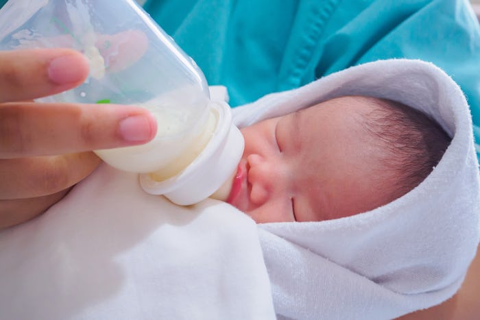 A closeup of a parent feeding a newborn from the bottle