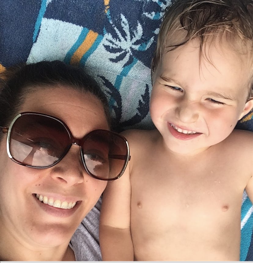 A mother is taking a picture with her toddler son out on a sunny day while lying on the towel