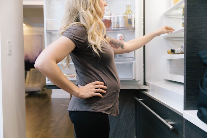 Pregnant woman standing in front of the fridge look for and craving red meat