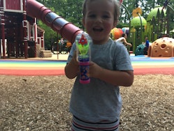 A toddler holding a plastic toy gun while standing in front of a playground