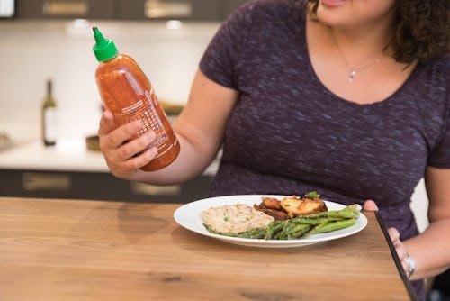 A pregnant woman indulging cravings with hot sauce bottle by meal.