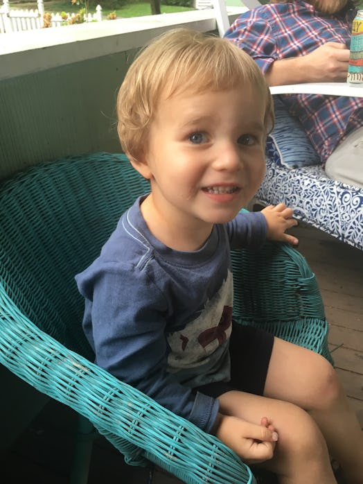 A smiling kid is sitting on a blue chair out on a porch. 