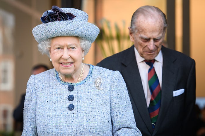 Queen Elizabeth in a light blue hat and matching dress with Prince Philip in a black suit walking be...