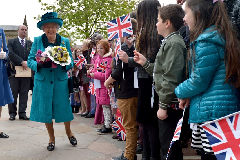 Queen Elizabeth walking with a flower bouquet surrounded by kids 