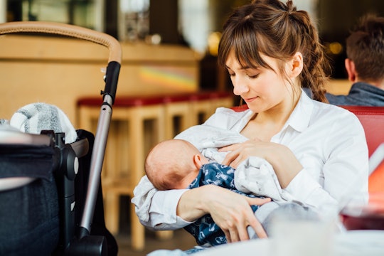 A woman breastfeeding her baby while sitting in a chair outside, with the stroller on the side