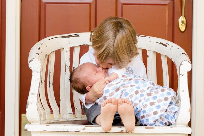 A woman's first kid, holding and kissing its sibling 