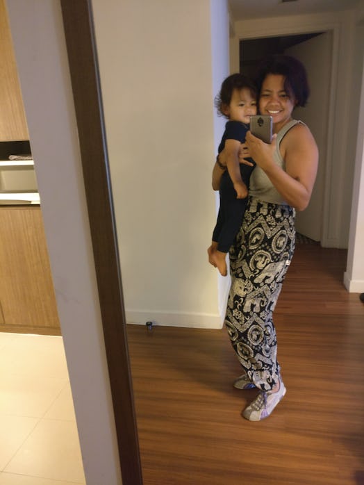 A mother taking a selfie carrying her child in her arms, wearing black and white elephant pants. 