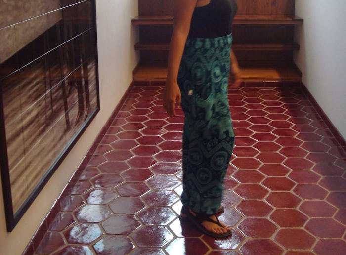 A woman in postpartum standing in a tiled hall while wearing a pair of cotton patterned pants