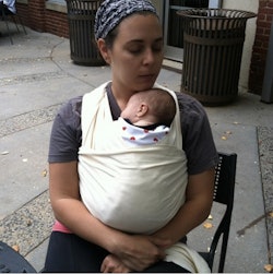 Sarah Bregel wearing a head band holding her baby in a baby carrier 