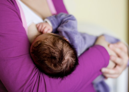 A mother in a purple shirt holding and breastfeeding her newborn baby