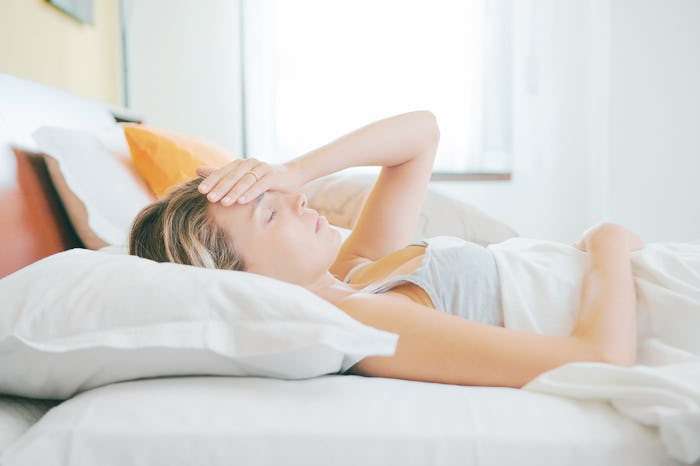 A pregnant woman lying in bed with a headache, holding her hand up to her forehead