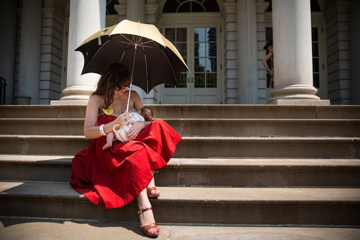 A woman in a red dress, holding an umbrella while sitting on the stairs and breastfeeding
