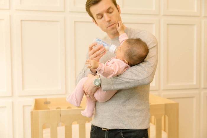 A man holding a baby while trying to feed her with a bottle