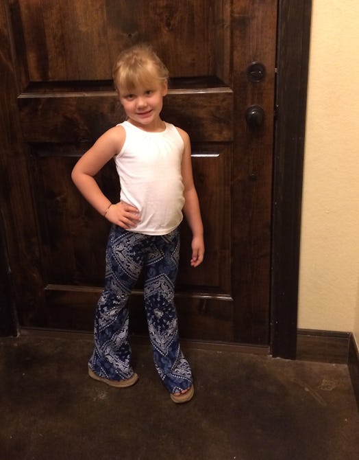 Little girl posing in front of the door wearing a white shirt and blueprint trousers.