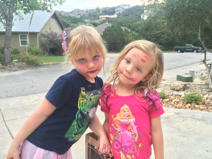 Two little girls wearing makeup are standing in the driveway, holding hands.