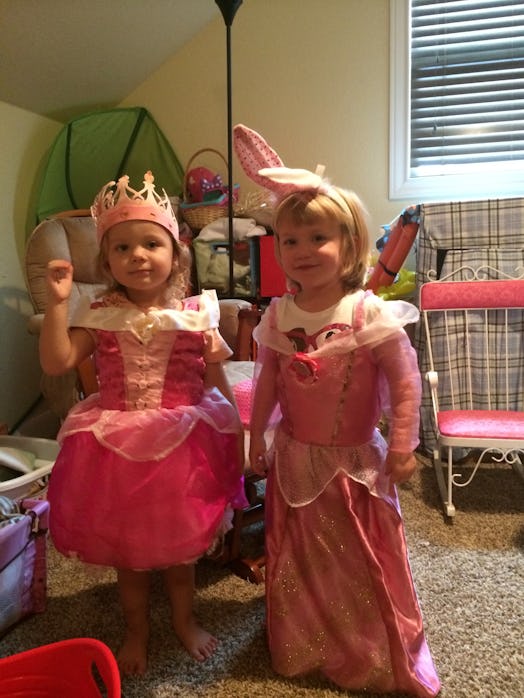Two little girls dressed as princesses smiling and posing for the picture in a room.