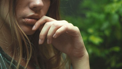 A woman leaning her hand against her lips while standing outside