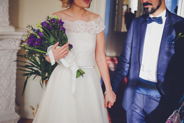 A bride carrying purple flowers and holding the grooms hand