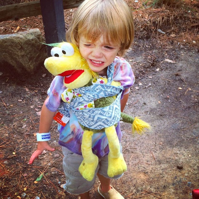 A little girl carrying a stuffed toy in a wrap on her chest 