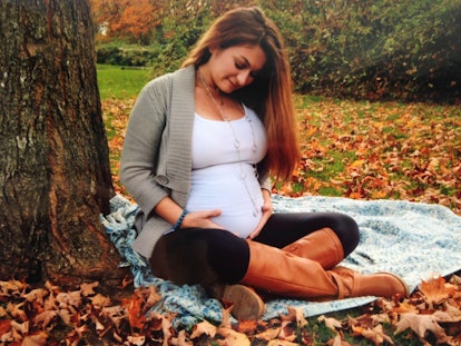 A pregnant lady posing outside, sitting on the ground on a beautiful autumn day