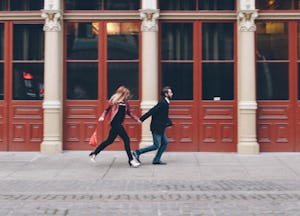 A couple of adults with ADHD holding hands while running on the sidewalk.