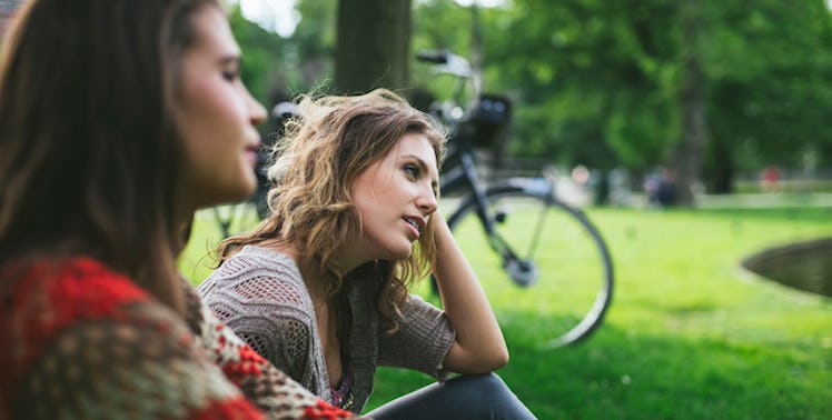 two women, suffering from depression, sitting in park on the grass.
