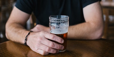 A man with alcohol addiction in a black shirt, leaning one arm on the table, and holding a glass of ...