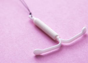 A white IUD placed on a pink surface