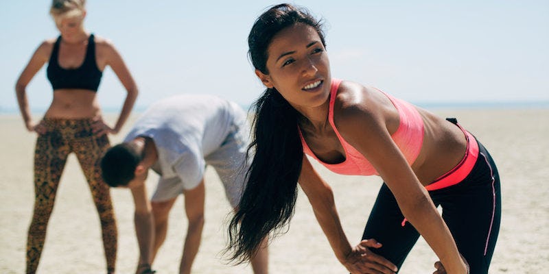 Two women and a man taking a break after jogging, doing a breathing exercise to lower stress levels 