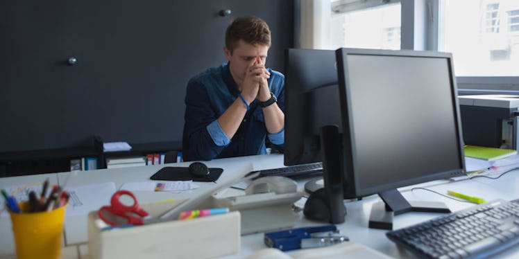 A man sitting in his office with his hands on his face, handling a stressful job