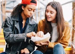 Two female friends eating chips from a cartoon box together