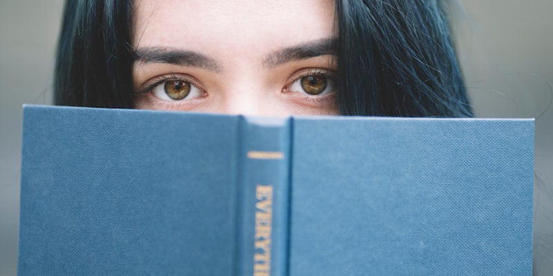 A dark haired woman peeking behind the book.