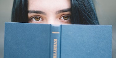 A dark haired woman peeking behind the book.